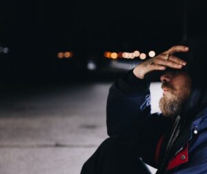man sits on street at night holding his face in his hand
