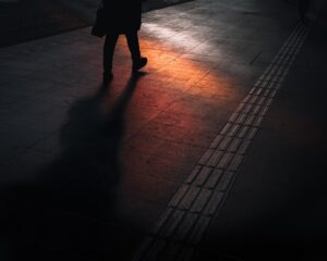 man walking on dark street with orange and red light reflecting off floor