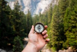 Hand holds compass with a view of forest and mountains