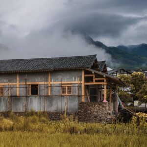 an almost-constructed traditional rural chinese house with misty hills in the background