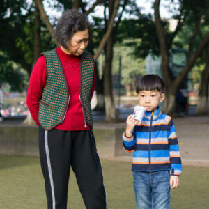 an older lady and a young boy stand together in a park