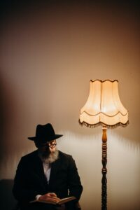 man in hat reads book by a lamp